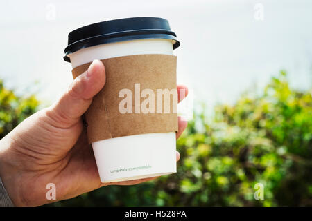 In prossimità di una mano umana in possesso di una carta monouso cup con un manicotto di cartone e coperchio in plastica. Foto Stock