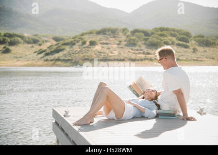 L uomo e la donna sdraiata su un molo, la lettura di un libro. Foto Stock
