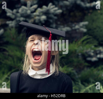 Ragazza in uniforme scolastica che indossa il cappuccio di graduazione grida Foto Stock