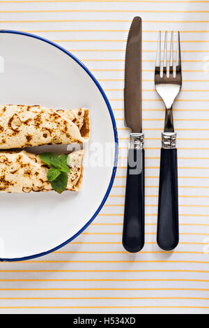 Frittelle sottili laminati crepes menta su una piastra con coltello e forchetta. Foto Stock
