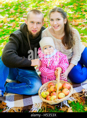 La famiglia felice avente un picnic con un bambino nel parco su una calda giornata d'autunno Foto Stock