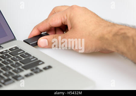 Una persona di sesso maschile di tamponamento dati USB stick viaggiatore in un notebook. closeup shot dal lato destro Foto Stock