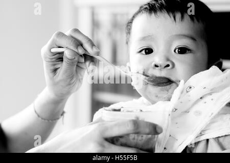 Baby cercando mentre l'alimentazione Mangiare sano cibo porridge, soft in bianco e nero a colori a basso tipo chiave. Foto Stock