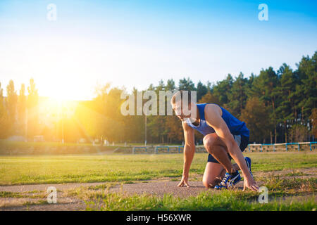 Uomo in bassa posizione di avviamento sul vecchio stadio. Atleta in posizione di partenza. In esecuzione, jogging, cardio, sport, stile di vita attivo concep Foto Stock