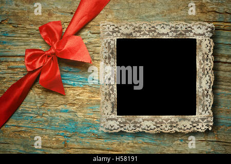 Un pizzo vuoto vintage photo frame sulla primitiva sfondo di legno e fiocco rosso Foto Stock