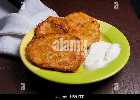 In casa frittelle di patate. Frittelle di patate con carne e panna acida sulla piastra verde su vintage marrone scuro dello sfondo. Foto Stock