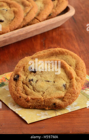 Freschi di forno biscotti con scaglie di cioccolato sul tovagliolo con vassoio di legno dei cookie in background in formato verticale. DOF poco profondo Foto Stock