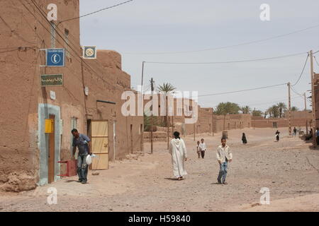 La strada principale di un piccolo deserto città nel deserto del Sahara, il sud del Marocco. Mostrato di mattoni di fango edifici e uomo in abito tradizionale Foto Stock