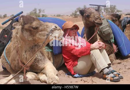 Un turista occidentale poggia, appoggiata contro un amichevole cammello durante un deserto trek nel sud del Marocco, Africa del Nord Foto Stock