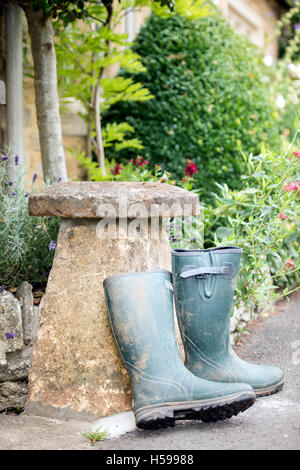 Un paio di stivali da pioggia appoggiata contro una pietra staddle al di fuori di un paese Cotswold cottage, REGNO UNITO Foto Stock