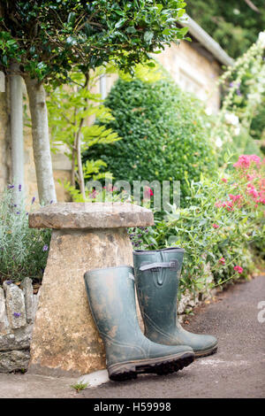 Un paio di stivali da pioggia appoggiata contro una pietra staddle al di fuori di un paese Cotswold cottage, REGNO UNITO Foto Stock