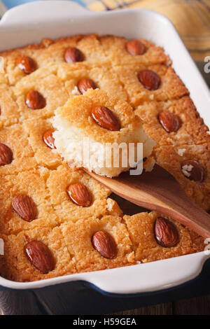 Torta Basbousa con mandorle macro in una teglia sul piano verticale. Foto Stock