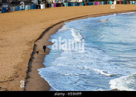 Una donna cammina il suo cane dal le onde che si infrangono sulla Broadstairs spiaggia sabbiosa, Kent, Regno Unito Foto Stock