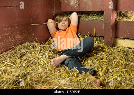 Ragazzo giovane reclino nel capannone di paglia, fattoria per bambini Kirchdorf, Amburgo, Germania Foto Stock