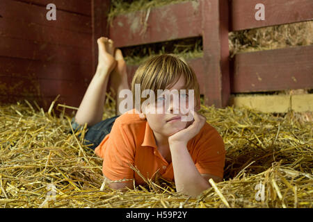 Ragazzo giovane reclino nel capannone di paglia, fattoria per bambini Kirchdorf, Amburgo, Germania Foto Stock