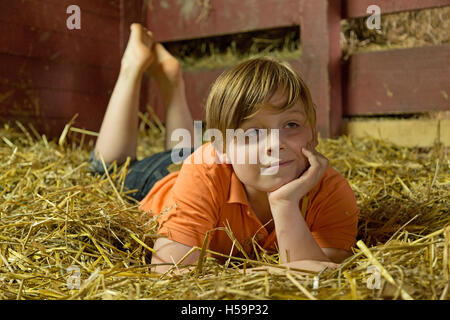 Ragazzo giovane reclino nel capannone di paglia, fattoria per bambini Kirchdorf, Amburgo, Germania Foto Stock