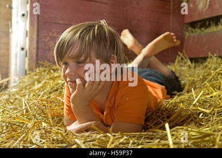 Ragazzo giovane reclino nel capannone di paglia, fattoria per bambini Kirchdorf, Amburgo, Germania Foto Stock