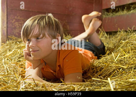 Ragazzo giovane reclino nel capannone di paglia, fattoria per bambini Kirchdorf, Amburgo, Germania Foto Stock