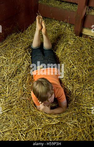 Ragazzo giovane reclino nel capannone di paglia, fattoria per bambini Kirchdorf, Amburgo, Germania Foto Stock