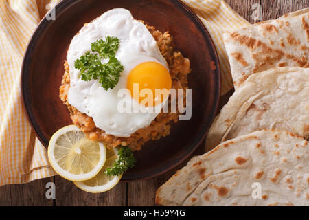 Ful medames con un uovo fritto e pane vicino sul tavolo. Vista orizzontale dal di sopra Foto Stock