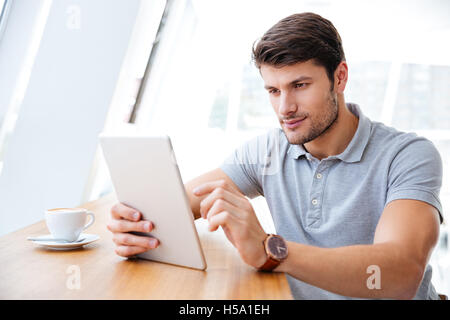 Giovane imprenditore in abiti casual con tavoletta e di bere il caffè in ambienti interni Foto Stock