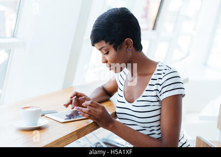 Attraente imprenditrice africana utilizzando tablet amd avente pausa caffè in ufficio Foto Stock