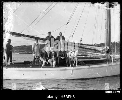 Un gruppo di otto uomini si vede posare su una barca, catturando un momento probabilmente dell'inizio del XX secolo. L'immagine riflette le attività sociali e la cultura della nautica da diporto del tempo, soprattutto in ambienti nautici. Foto Stock