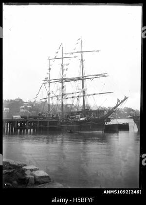 Questa immagine presenta una barca a tre alberi, un tipo di nave a vela, ormeggiata lungo un molo. Gli alti alberi e le attrezzature della nave sono caratteristiche delle tradizionali navi a vela utilizzate per il trasporto merci e passeggeri nel XIX e all'inizio del XX secolo. Foto Stock