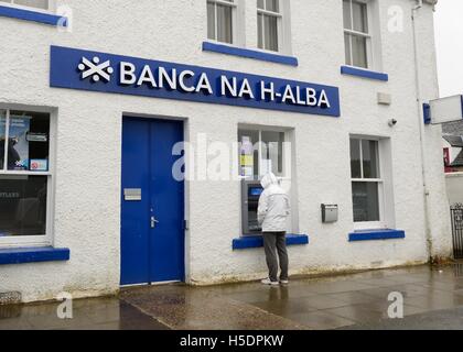 Un uomo di prelevare denaro dal bancomat presso Bank of Scotland recanti il nome in gaelico sull'Isola di Skye in Scozia, Regno Unito Foto Stock