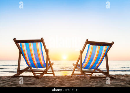 Due sedie a sdraio su una spiaggia sabbiosa tropicale con un bellissimo tramonto colorato Foto Stock