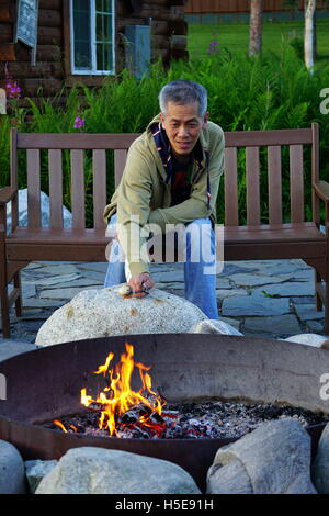 Uomo asiatico la tostatura marshmallow in un metallo una buca per il fuoco (falò) a Mt. McKinley Princess Wilderness Lodge nel Denali, Alaska Foto Stock