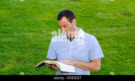 L'uomo della lettura della Bibbia al di fuori seduta con erba in background. Foto Stock