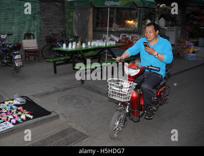 Un uomo cinese sta parlando sul suo smartphone durante la guida di un scooter. Vicino l'Houhai Lake, Pechino, Cina. 25.04.2016. Foto Stock