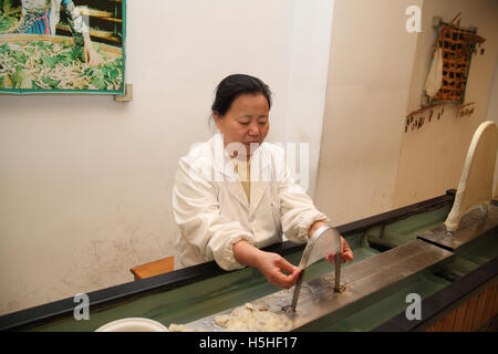 Un lavoratore di sesso femminile si estende su un arco di metallo del tessuto usato per essere il bozzolo è fatto in una tradizionale fabbrica di seta, Suzhou, Cina. Foto Stock