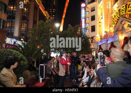 Donna canta le altre persone ad ascoltare i suoi sulla moda Nanjing Street in una serata di un weekend di vacanza. Shanghai, Cina Foto Stock