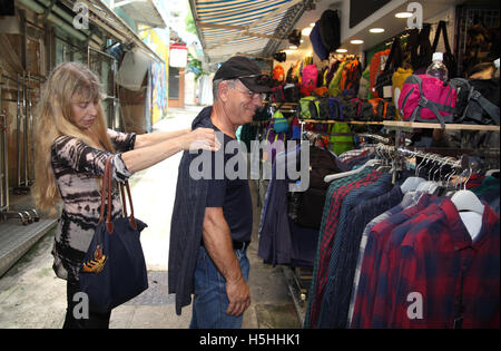 A sessant anni vecchia donna, mette un plaid shirt sulle spalle del suo sorridente 59 anno vecchio amico, per vedere se si inserisce prima dell'acquisto. Stanley Village, Hong. Foto Stock