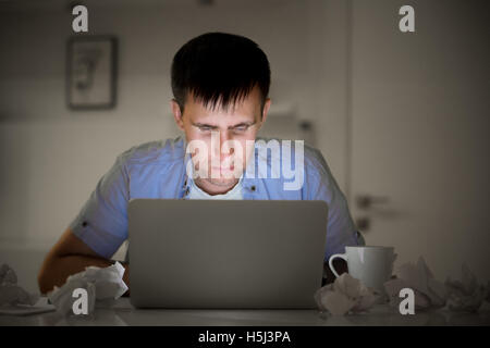 Ritratto di un uomo con un computer portatile a tarda notte, la luce dello schermo Foto Stock