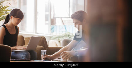 Colpo di due giovani imprenditori seduti insieme in un bar e a lavorare su un nuovo progetto di business. I dirigenti riuniti in ufficio lo Foto Stock