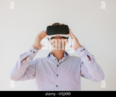 Colpo di giovane imprenditore guarda il contenuto su una realtà virtuale auricolare. Modello maschile con la realtà virtuale occhiali protettivi contro grigio ba Foto Stock