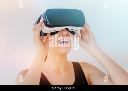 Immagine ravvicinata di sorridere giovane donna utilizzando il VR occhiali protettivi contro uno sfondo grigio con la sunflare effetto. Asian modello femminile weari Foto Stock