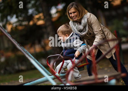 Madre giocando con il figlio sulla giostra all'aperto Foto Stock