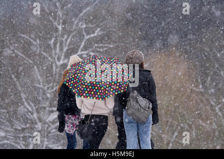 Ragazze raggomitolati insieme sotto l ombrello coloratissimo nella neve pesante, Christchurch Park, Ipswich, Suffolk, Gennaio 2010 Foto Stock