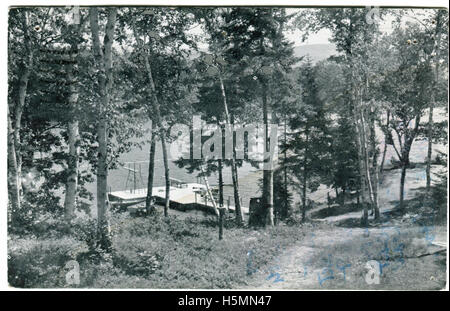 Una vera cartolina foto di Camp Merestead in Camden, Maine. La foto mostra un dock su un lago, con due schede di immersioni. Una piccola barca è prossima al dock. Il percorso si snoda lungo il lago. Camp Merestead è stato costruito sulle rive del lago Megunticook in Camden come una ragazza camp negli anni trenta. La proprietà attualmente appartiene alla diocesi di Espiscopal, e viene gestito come un co-ed accampamento chiamato Bishopswood Camp. Foto Stock