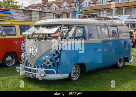 Una luce blu a schermo diviso VW camper van drappeggiati con Cornish bandiere in mostra a Paignton verde con altri veicoli Foto Stock