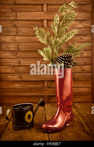 Sfondo di natale, stivali da pioggia e annaffiatoio in legno rustico sfondo Foto Stock