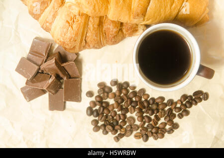 Croissant al cioccolato, una tazza di caffè e caffè in grani Foto Stock