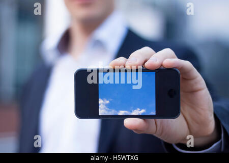 Imprenditore che mostra lo schermo dello smartphone con edifici per uffici in background Foto Stock