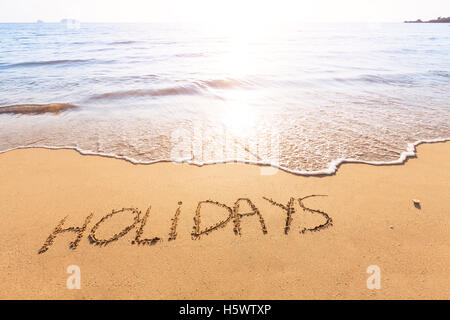 Vacanze a testo scritto nella sabbia di una spiaggia tropicale con luce solare Foto Stock