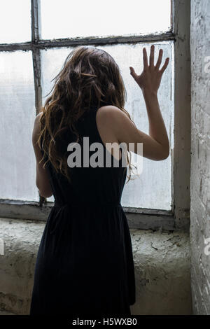 Vista posteriore di una giovane donna in piedi dalla finestra Foto Stock