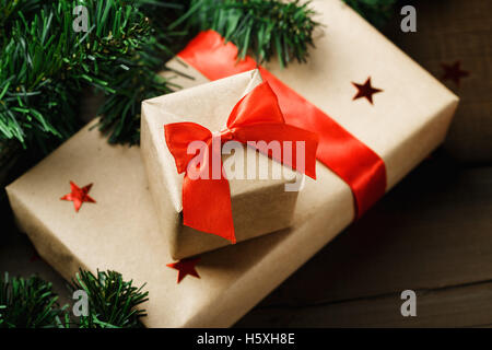 Close-up di regali di Natale avvolti in carta craft con la festosa nastri rossi tra il verde di rami di abete. Concetto di Natale per il messaggio di saluto Foto Stock
